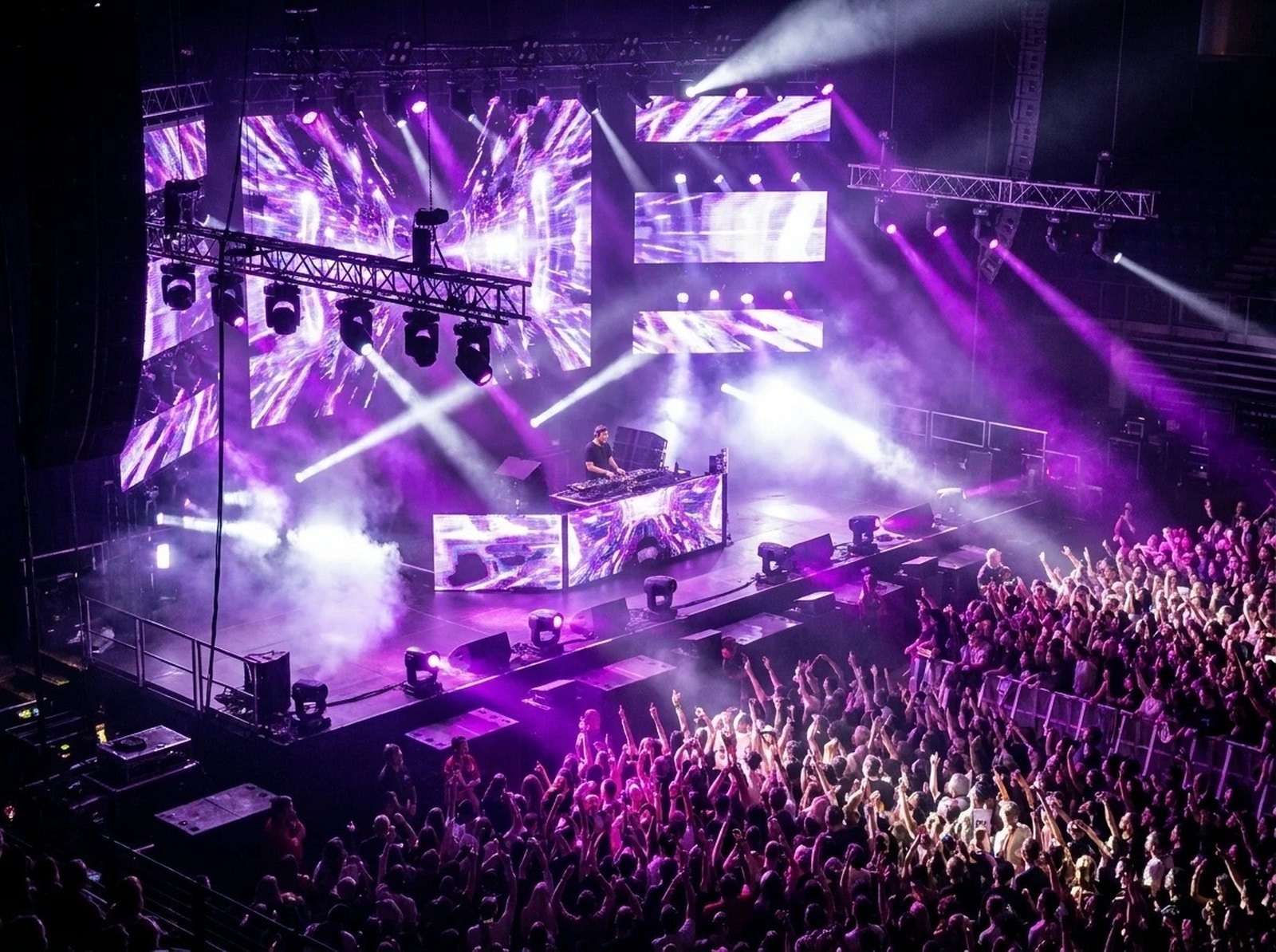 DJ performing to a packed arena crowd under purple stage lighting