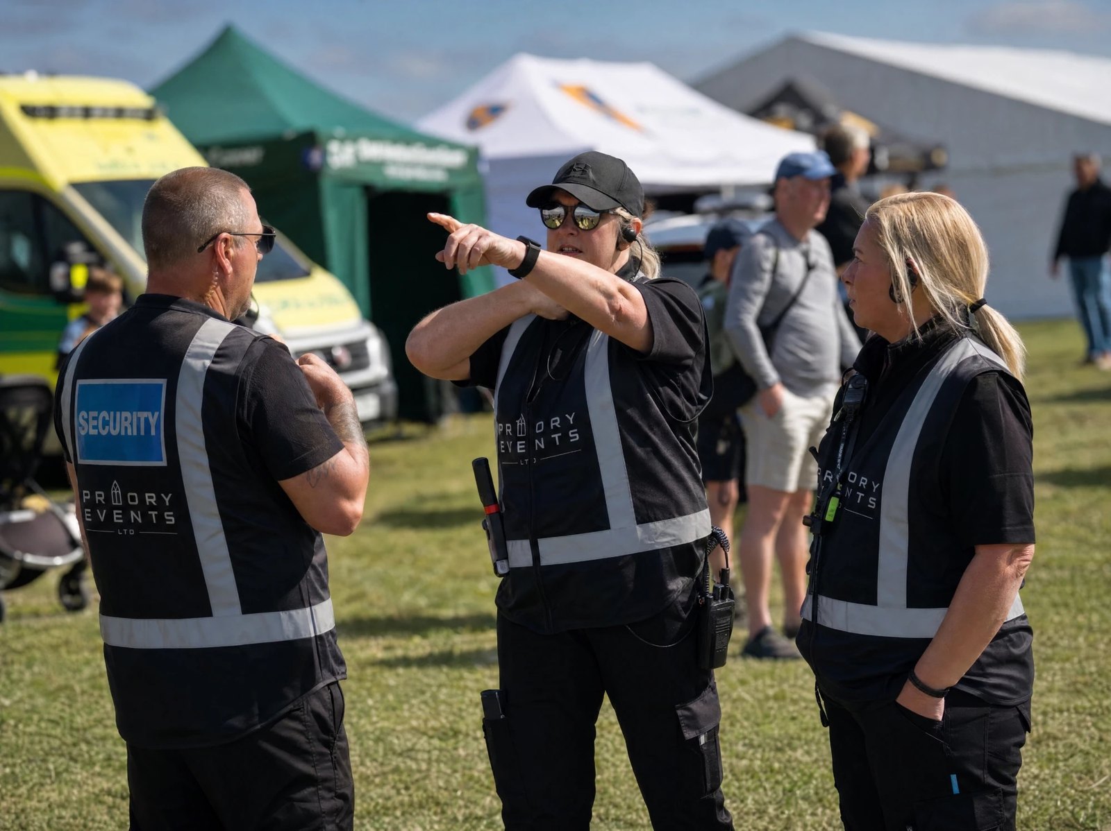 Three Priory Events security staff in branded vests briefing at an outdoor event